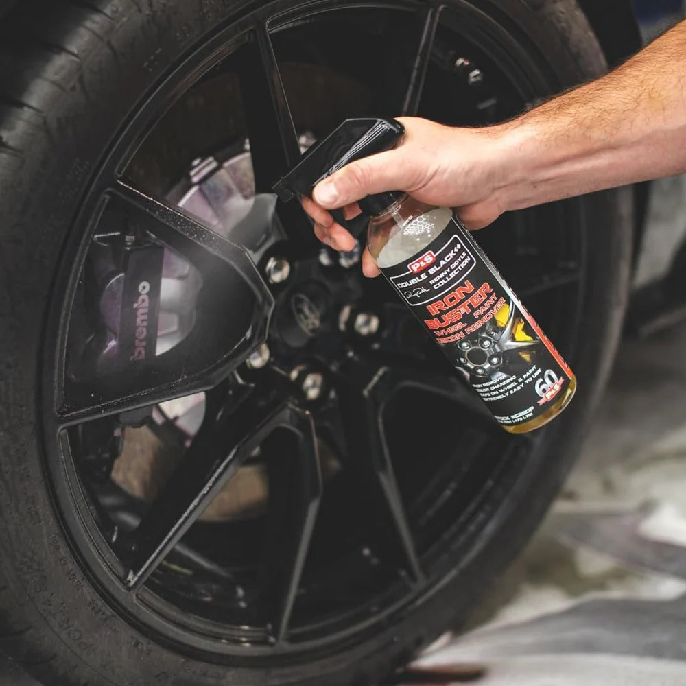 Hand holding iron remover spray bottle over a black wheel rim