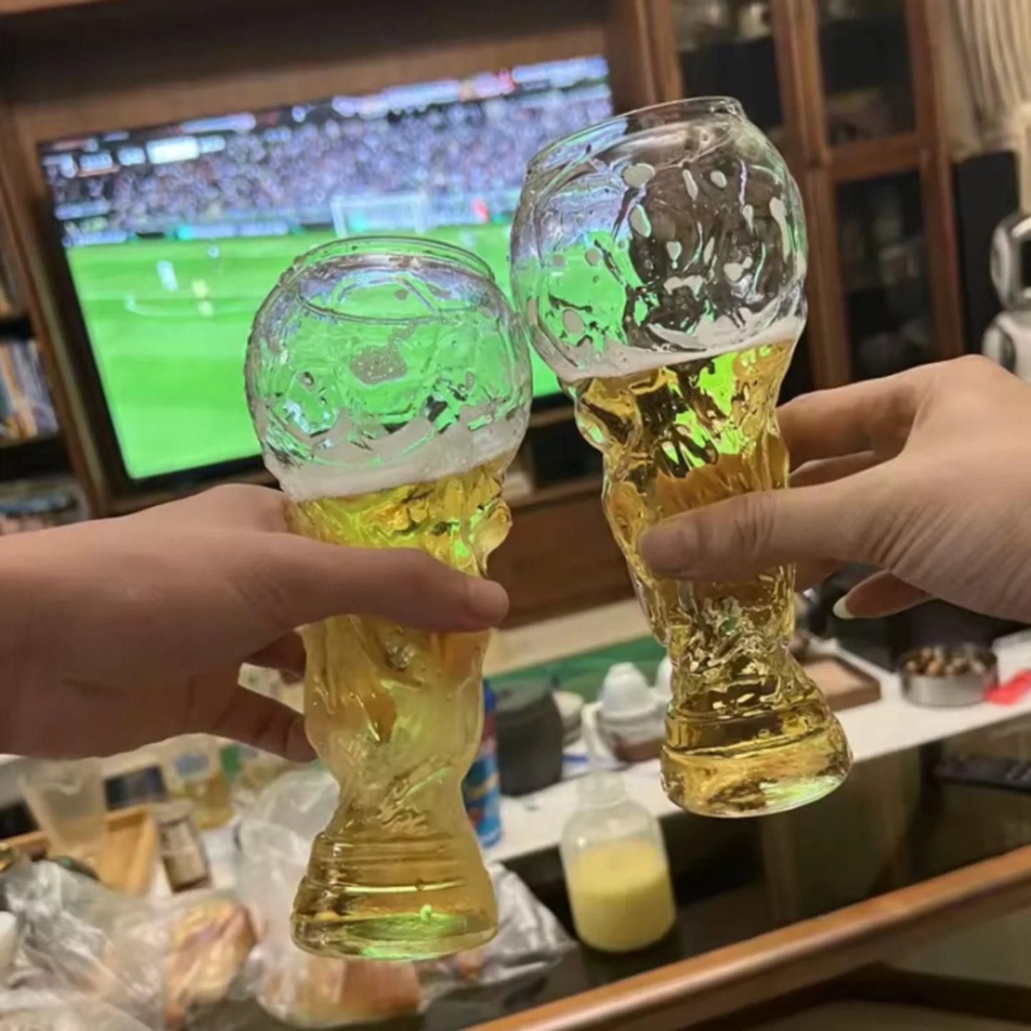 Crystal trophy glasses held up, one with amber beer and one with green-tinted drink